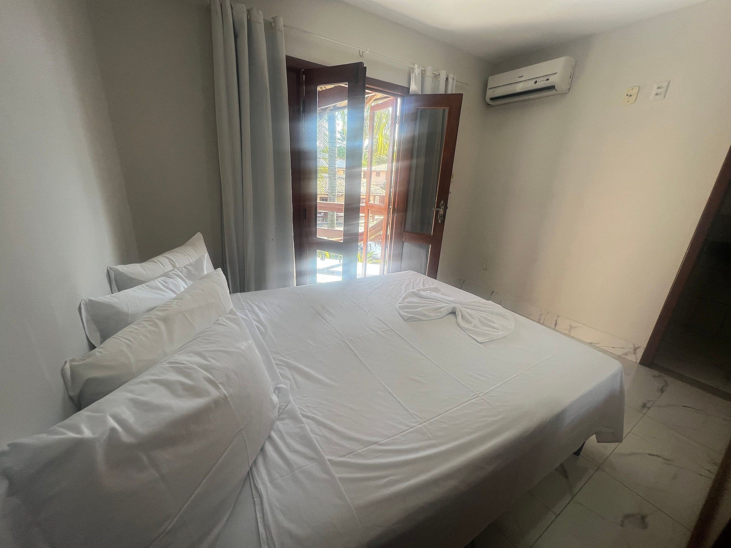 A hotel room with a bed, curtains, an air conditioning unit, and a view through a door.