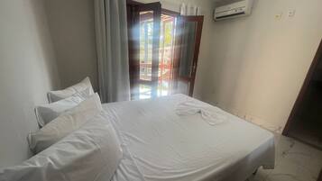A hotel room with a bed, curtains, an air conditioning unit, and a view through a door.