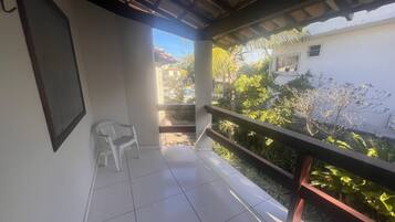 Ein Balkon mit einem Stuhl und Blick auf einen Garten, im Hintergrund ein Gebäude.