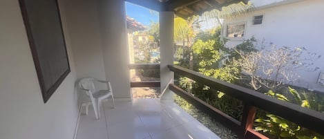 Un balcón con una silla y vista a un jardín, con un edificio al fondo.