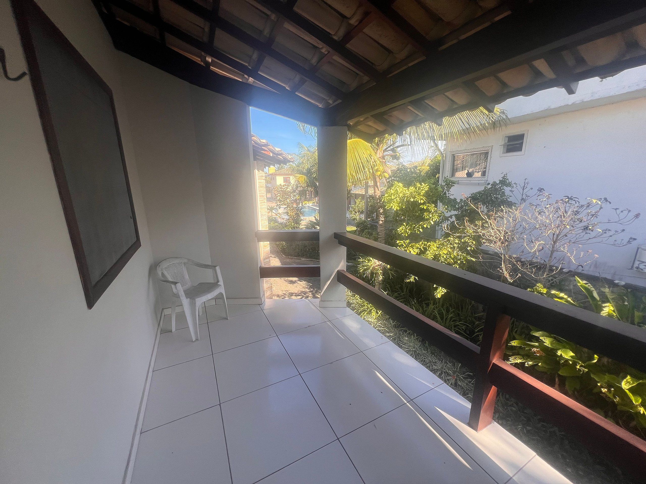 En balkon med en stol, udsigt over en have og en bygning i baggrunden.