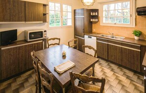A kitchen with wooden cabinets, a dining table with chairs, a microwave, a dishwasher, and a window with a view of greenery.