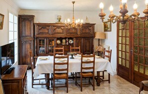 A dining room with a large table set for six, wooden cabinets, a chandelier, and a television on the left.