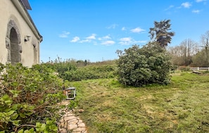 A stone pathway leading to a building with an arched entrance, surrounded by greenery and a clear sky.