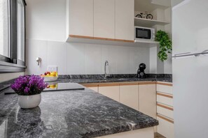 A modern kitchen with a granite countertop, white cabinets, a microwave, a coffee maker, and a potted plant. - MOT Rentals MusikHaus Soho 4Bd 10pax (Buenos Aires)