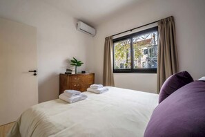 A hotel room with a bed, a dresser, a window with curtains, and an air conditioning unit. - MOT Rentals MusikHaus Soho 4Bd 10pax (Buenos Aires)