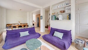 A living room with two purple sofas, a small green table, and a bookshelf with books and decorative items. - La Maison Raspail - Welkeys (Bois-Colombes)