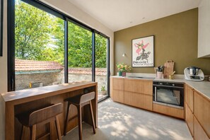 Une cuisine moderne dotée d’une grande fenêtre, de meubles en bois, d’un four encastré et d’un coin repas avec deux chaises.