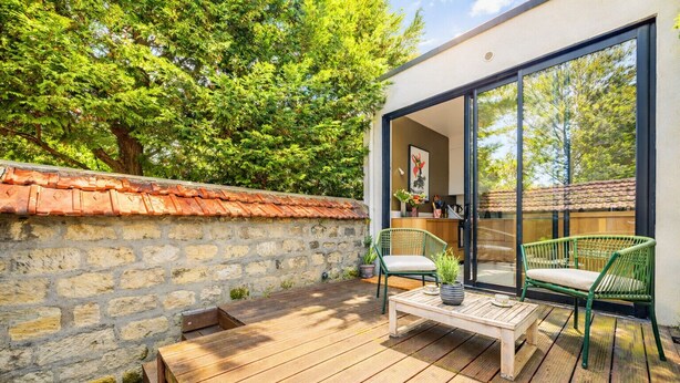 A wooden deck with a stone wall, two wicker chairs, and a table with a potted plant. - La Maison Raspail - Welkeys (Bois-Colombes)