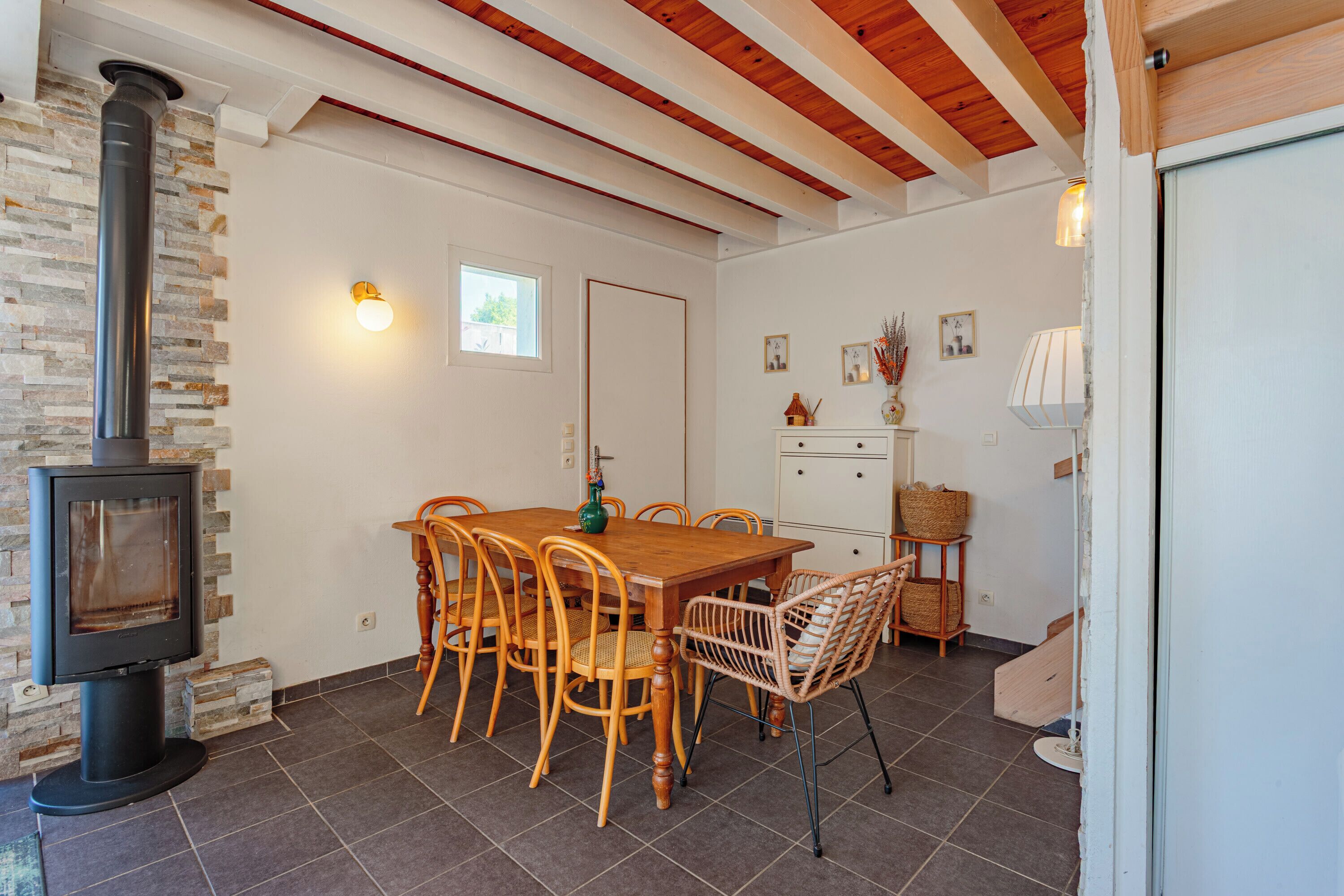 Un espace repas comprenant une table et des chaises en bois, un mur en pierre, une cheminée et une porte.