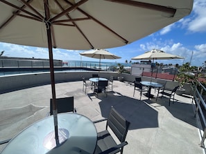 Um terraço no telhado com área de estar externa, piscina e vista para o mar.