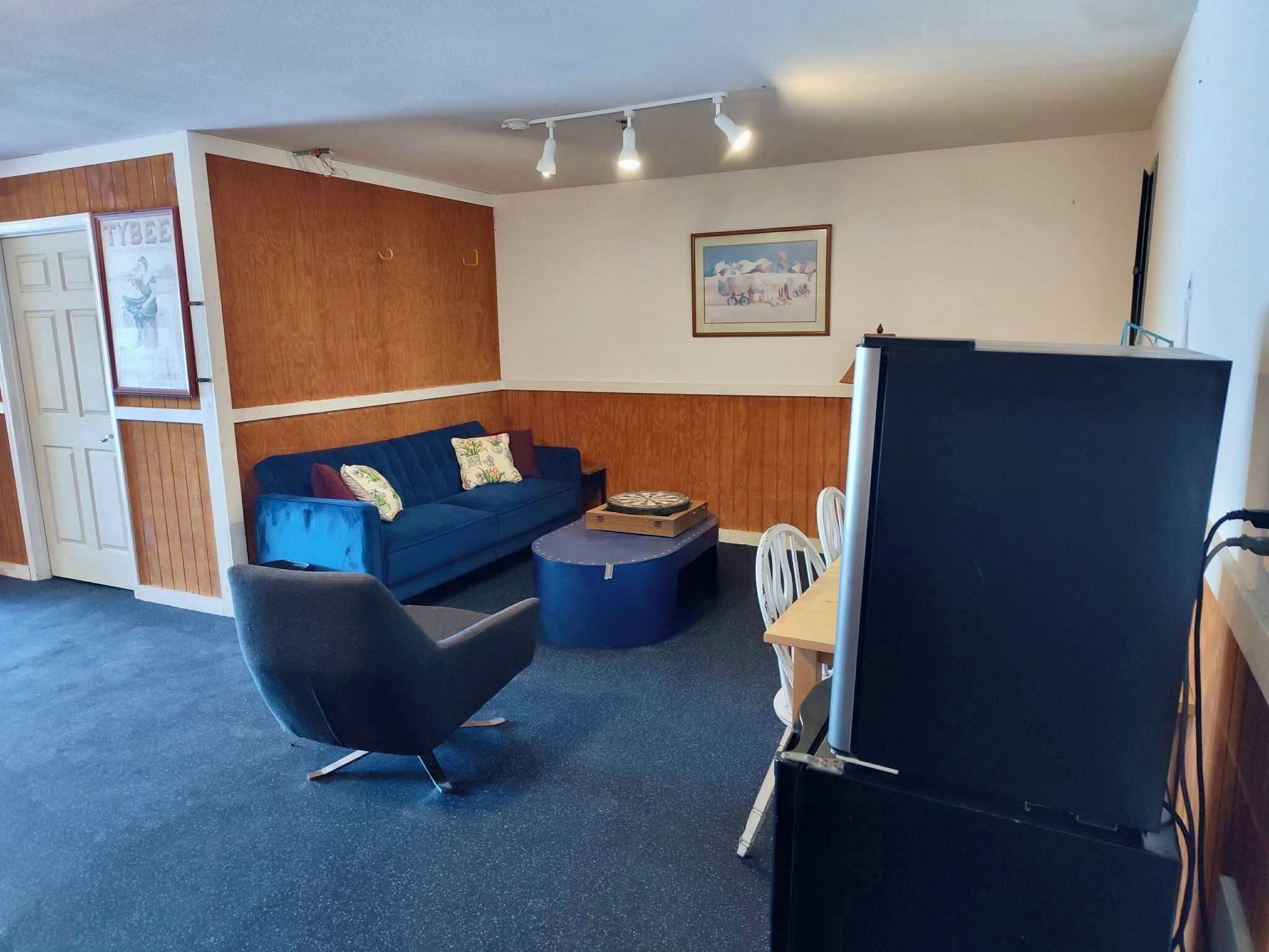 A room with a blue sofa, a black chair, a small round table, and a television.