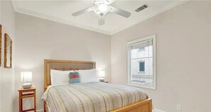 Un dormitorio con cama, lámparas de noche, ventilador de techo y ventana.