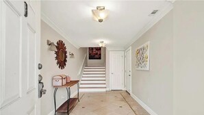 Un couloir avec un escalier, des murs blancs et un luminaire.