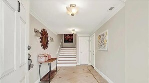 A hallway with a staircase, white walls, and a light fixture. - Steps from the sand. Miles from stress. (Tybee Island)