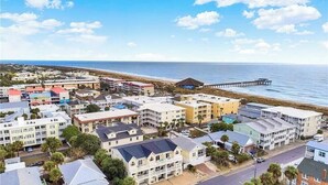 Une ville côtière avec des bâtiments, une jetée qui s’avance dans la mer et un ciel dégagé.