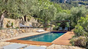 Ein rechteckiger Pool mit Holzterrasse, Steinmauern und Liegestühlen.