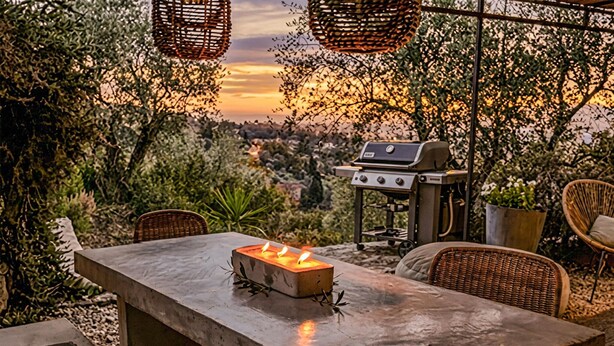 Eine Außenpatio mit einem Betontisch, Korbstühlen, einem Grill und Blick auf die Landschaft.