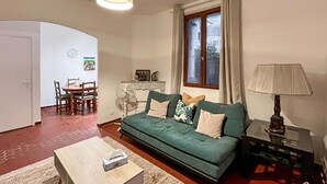 A living room with a green sofa, a wooden coffee table, a lamp, a fan, and a dining area with chairs and a table. - 3 bedroom pet friendly home in Vence (Vence)