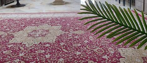 Una habitación con alfombra estampada, un sofá, una mesa, una fuente y una zona de estar con sillones.