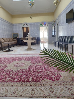 A room with a patterned carpet, a sofa, a table, a fountain, and a seating area with chairs.