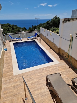 A rectangular swimming pool with two lounge chairs, a hose, and a view of the sea.