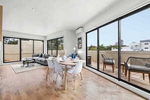 A spacious living area with a dining table, sofas, and large windows offering a view of the city. - LaneStay - 3B2B Bright Apartment with Free Parking (St Kilda)
