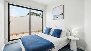 Een slaapkamer met een bed, nachtkastje, schilderij en een schuifdeur naar een balkon.