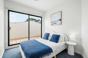 Un dormitorio con una cama, una mesita de noche, un cuadro y un ventanal corredero a un balcón.
