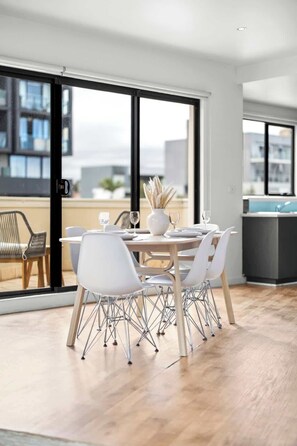 Comedor con una mesa preparada para cuatro personas, un florero con plantas secas y vista a través de puertas corredizas de vidrio.