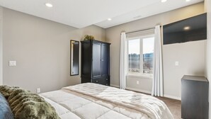 Een slaapkamer met een bed, een kledingkast, een televisie en een raam met gordijnen.