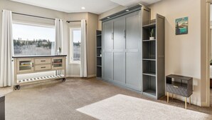 Een kamer met een grote grijze garderobe, een wit bureau en een raam met gordijnen.