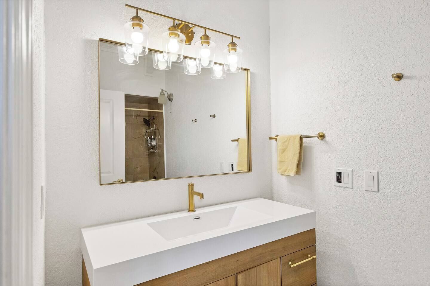 A bathroom with a white sink, gold faucet, and a mirror with light fixtures.