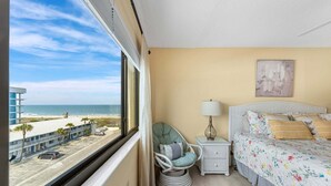 Camera d'albergo con un letto, una sedia, un comodino, una lampada e vista sulla spiaggia.