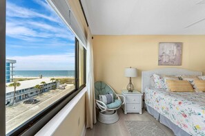 A hotel room with a bed, a chair, a nightstand, a lamp, and a view of the beach. - Gorgeous Cocoa Beach Condo with Private Balcony Heated Pool & Hot Tub! ☀️ (Cocoa Beach)