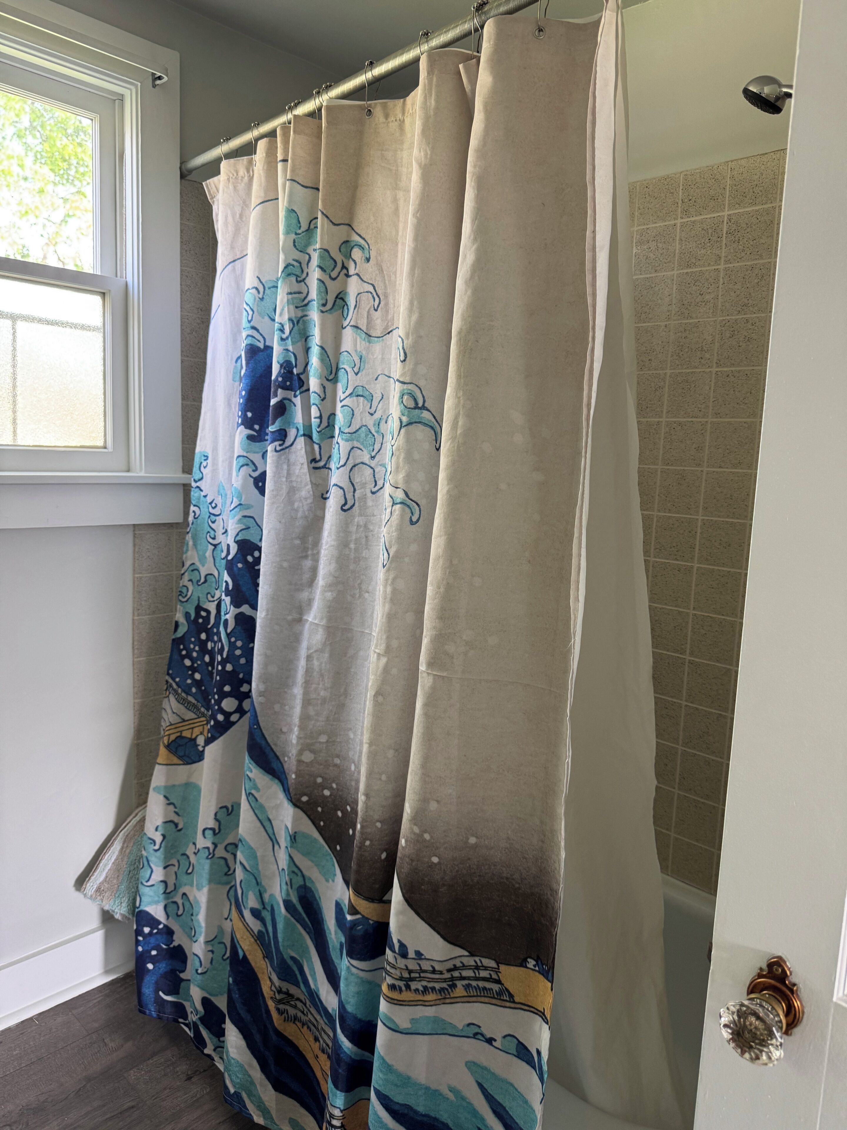 Un baño con cortina de ducha estampada con un motivo de olas, una ventana y una pared de azulejos.