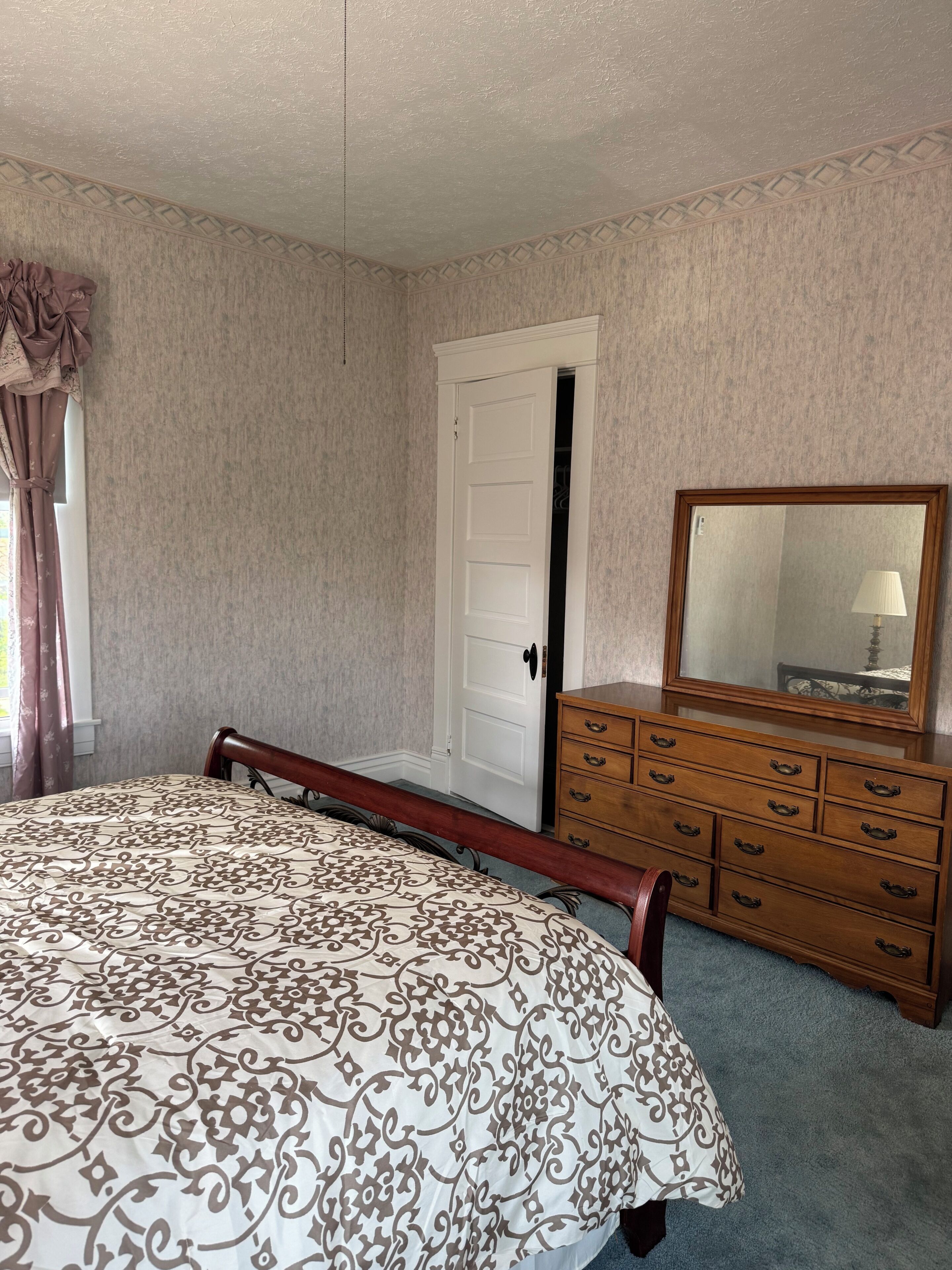 Un dormitorio con cama, cómoda, espejo y puerta.