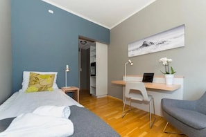 Ein Hotelzimmer mit Bett, Schreibtisch, Laptop, Stuhl und einem Gemälde an der Wand.