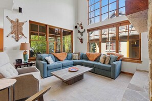 A spacious living room with a sectional sofa, a coffee table, and large windows. - Luxury Timbers Townhome | Walk to Town & Ski (Ketchum)