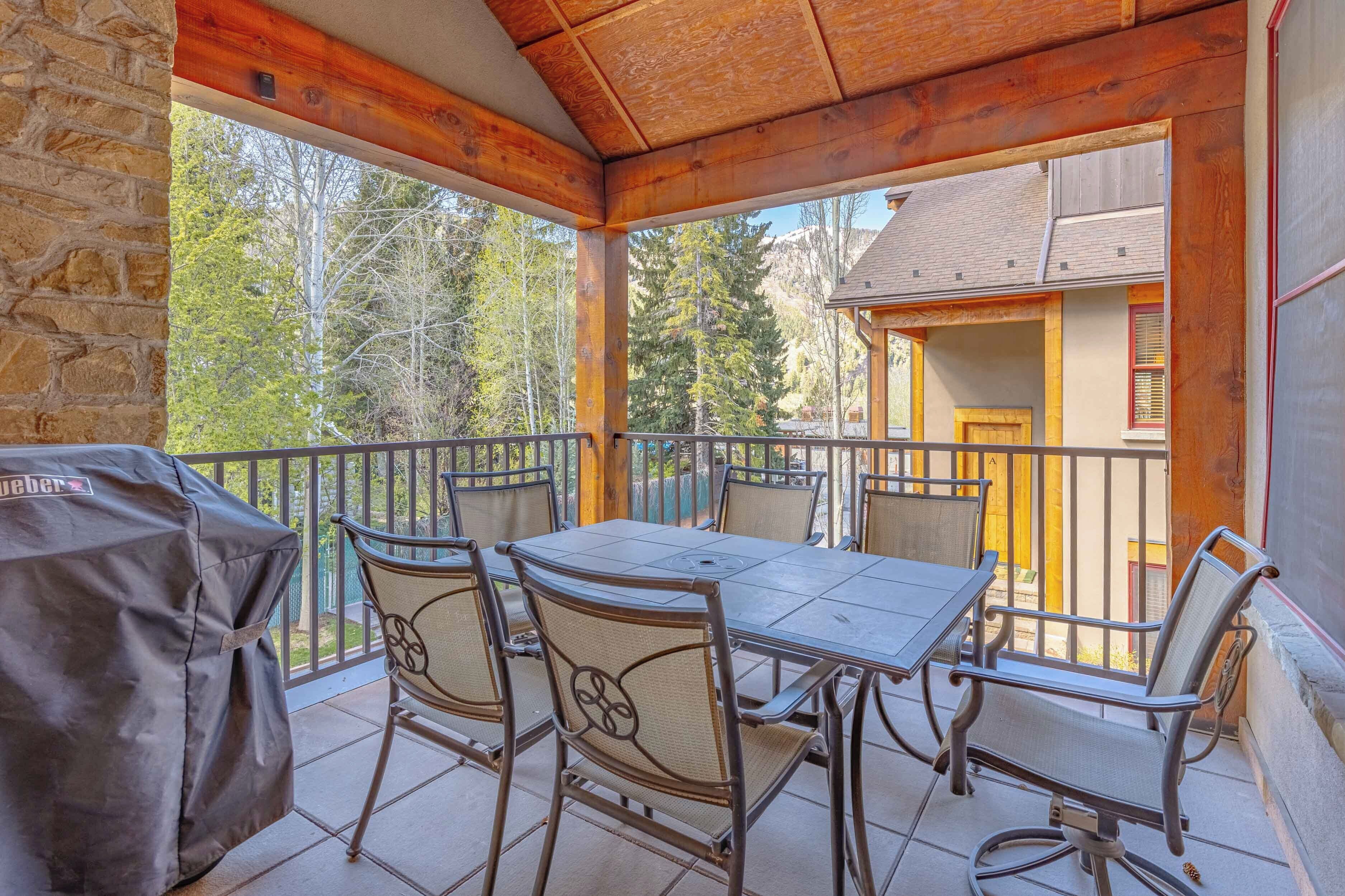 Un patio couvert avec une table et des chaises, un barbecue et une vue sur une montagne et des arbres.