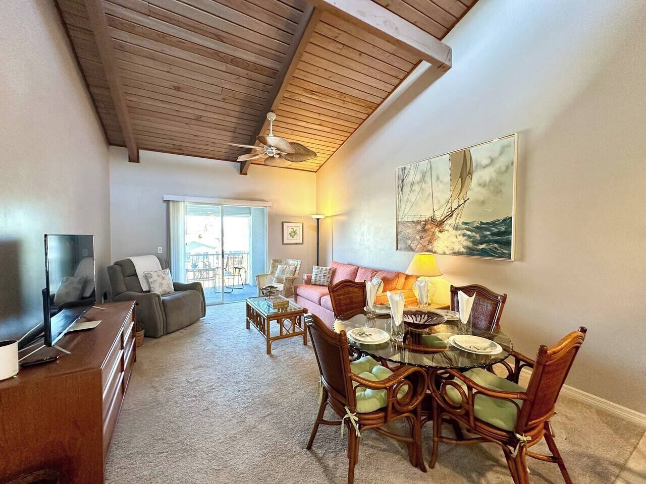 A living room with a TV, sofa, dining table, chairs, and a ceiling fan.
