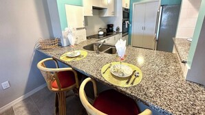 Une cuisine dotée de plans de travail en granit, de meubles blancs et d’un réfrigérateur en acier inoxydable.