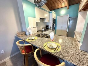 A kitchen with granite countertops, white cabinets, and a stainless steel refrigerator. - Spot manatees from your balcony (Englewood)
