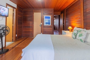 Una habitación con paneles de madera, una cama, un ventilador, un televisor y una lámpara.
