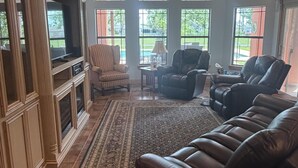 Ein geräumiges Wohnzimmer mit einer großen Ledersofa, einem Fernseher und einem Deckenventilator.