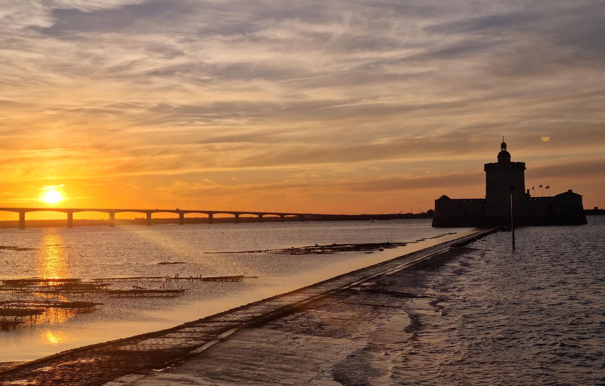 Un coucher de soleil sur une rivière, avec un pont et une tour.
