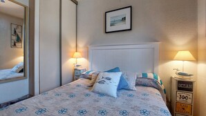 A bedroom with a bed, two bedside lamps, a framed picture, and a nightstand with a sign.