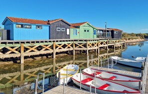 A pier with colorful wooden buildings, a dock with boats, and calm water. - Appartement proche plage (Saint-Georges-de-Didon)