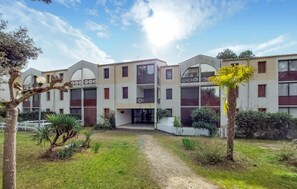 A multi-story building with balconies, a central entrance, and a surrounding garden with trees and shrubs. - Appartement proche plage (Saint-Georges-de-Didon)