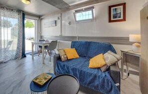 Ein Zimmer mit einer Couch, einem Esstisch und einem Stuhl. Es gibt ein Fenster mit Jalousien, ein Bild an der Wand und eine Lampe auf einem Beistelltisch.